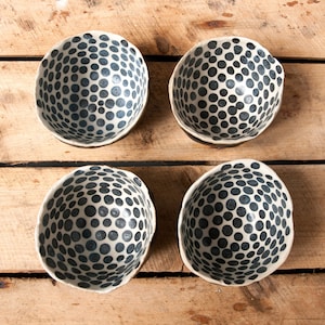 May include: Four white ceramic bowls with a black polka dot pattern. The bowls are arranged in a square pattern on a wooden surface.