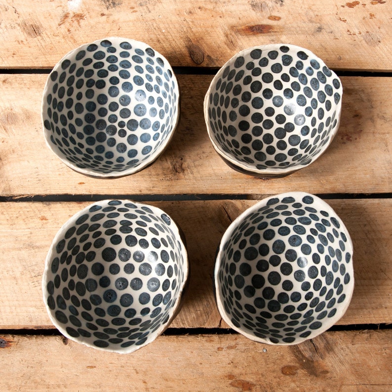 May include: Four white ceramic bowls with a black polka dot pattern. The bowls are arranged in a square pattern on a wooden surface.