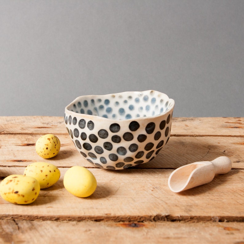 May include: A white ceramic bowl with a black and blue polka dot pattern. The bowl is sitting on a wooden surface with four yellow speckled eggs.