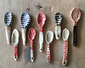 May include: A set of ten ceramic spoons with polka dot patterns in blue, red, and black. The spoons are hand-painted and have a white background.