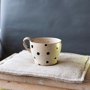 May include: A speckled beige ceramic mug with a black polka dot pattern and a rounded handle.