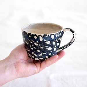 May include: A white ceramic mug with a black abstract design. The mug has a rounded shape and a handle.