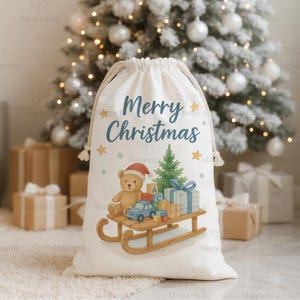 Peut inclure: Un sac cadeau de No&euml;l blanc avec l'inscription "Merry Christmas" en bleu. Le sac pr&eacute;sente un ours en peluche avec un bonnet de P&egrave;re No&euml;l, un sapin de No&euml;l et des jouets sur une luge en bois. Des &eacute;toiles et des flocons de neige ornent le design.