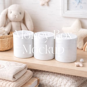 Puede incluir: Tres huchas cilíndricas blancas con una ranura en la parte superior, dispuestas sobre una estantería de madera clara. El texto "Money Box Mockup" está impreso en las huchas. Un conejito de peluche y otra decoración de guardería están en el fondo.