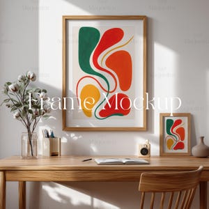 May include: A wooden desk with a chair, a vase of cotton flowers, a framed abstract painting with red, orange, yellow, and green shapes, a small framed abstract painting, a notebook, a pen, and a small wooden box.