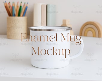 May include: A white enamel mug with a silver rim and handle. The mug has the words "Enamel Mug Mockup" printed on the front. The mug is on a white surface with pencils, books, and a wooden rainbow in the background.