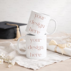 Pode incluir: Duas canecas de cerâmica brancas empilhadas, cada uma com o texto "your design here" em marrom. Uma touca de formatura e um diploma enrolado com uma fita estão ao fundo.