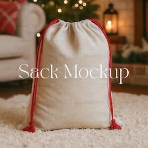 May include: A beige drawstring sack with red rope ties and tassels. The words "Sack Mockup" are printed on the front of the sack. The sack is sitting on a white, fluffy rug, with a blurred background of a Christmas tree and a lantern.
