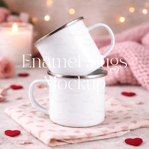 May include: Two white enamel mugs with silver rims are stacked on a pink heart-patterned napkin. The mugs have white handles. The image includes the text "Enamel Mugs Mockup". Red heart-shaped decorations are scattered around.