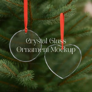 Puede incluir: Dos adornos de cristal transparente, uno redondo y otro en forma de corazón, cuelgan de cintas rojas sobre un fondo de agujas de pino verdes. El texto "Crystal Glass Ornament Mockup" se muestra.