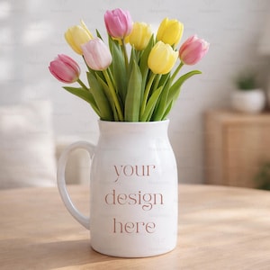 Könnte beinhalten: Eine weiße Keramikkrug mit Henkel, gefüllt mit einem bunten Tulpenstrauß. Die Tulpen sind rosa, gelb und weiß, mit grünen Stielen und Blättern. Auf dem Krug steht der Text "your design here".