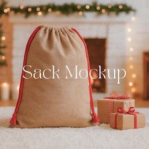 May include: A tan burlap sack with red drawstring and trim, labeled "Sack Mockup". Two wrapped gifts with red ribbon are in the background. The scene is set in front of a fireplace with soft lighting, suggesting a holiday theme.