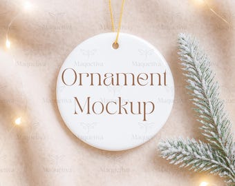 Könnte beinhalten: Ein weißer, runder Ornament-Mockup mit dem Text "Ornament Mockup" in Braun. Das Ornament hängt an einem goldenen Faden. Ein Zweig eines gefrosteten Nadelbaumzweigs und Lichterketten befinden sich im Hintergrund.