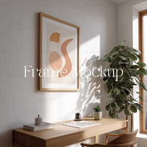May include: A wooden desk with a framed abstract art print, a potted plant, and a stack of books. The desk is in a room with a window and white walls.  Frame Mockup