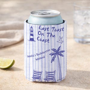 May include: A blue and white striped can cooler with the text "Last Toast On The Coast" and "Amelia's Bachelorette Weekend". The design includes a lighthouse, palm tree, bird, and beach chairs. A light blue can is inside the cooler.