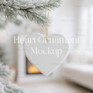 Può includere: Un ornamento bianco a forma di cuore è appeso a un filo d'oro su uno sfondo sfocato. L'ornamento presenta la scritta "Heart Ornament Mockup". È appeso davanti a un ramo di sempreverde ghiacciato.