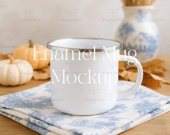 May include: A white enamel mug with a silver rim, resting on a blue and white patterned cloth. The mug has the text "Enamel Mug Mockup" on it. Two pumpkins and a vase with wheat stalks are in the background.