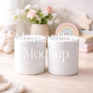 Könnte beinhalten: Zwei weiße zylindrische Spardosen mit einem Schlitz oben, beschriftet mit "Money Box Mockup" in einer weichen Schriftart. Der Hintergrund umfasst einen Teddybären, Blumen und eine regenbogenförmige Dekoration.