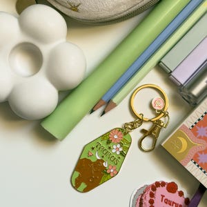 May include: A collection of stationery items including pencils, a flower-shaped object, and a Taurus keychain. The keychain is green with a brown bull illustration and the word "Taurus". A small cake sticker with the words "Taurus baby" is also visible.