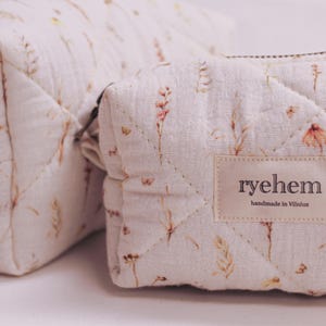 Könnte beinhalten: Zwei gesteppte Kosmetiktaschen mit einem floralen Muster in Beige, Braun und Rosa. Die kleinere Tasche hat einen Reißverschluss und ein Etikett mit der Aufschrift "ryehem handmade in Vilnius."