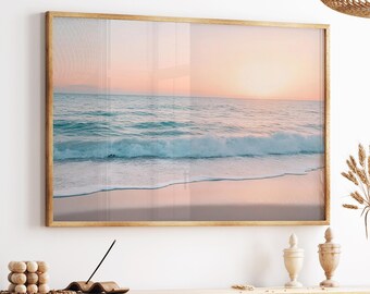 May include: A rectangular framed wall art print featuring a serene coastal landscape at sunset. The image displays a calm ocean with gentle turquoise waves rolling onto a sandy beach under a soft, gradient sky of pale pink and warm orange hues.