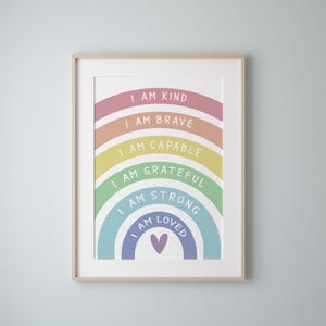 Puede incluir: Impresión artística enmarcada con un diseño de arcoíris y las frases "I AM KIND", "I AM BRAVE", "I AM CAPABLE", "I AM GRATEFUL", "I AM STRONG" y "I AM LOVED". Un corazón morado en la parte inferior. El marco es de madera clara.