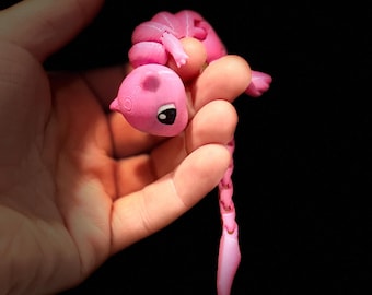 May include: A pink, segmented, hand-painted, articulated toy creature with a curled tail and large eyes.