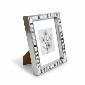 Può includere: Una cornice argentata con un bordo a mosaico di piastrelle rettangolari bianche, grigie e nere. La cornice contiene una stampa floreale in bianco e nero ed è sostenuta da un cavalletto marrone.