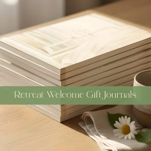 May include: A stack of cream-colored journals with a soft-focus illustration of a window and curtains on the cover. The text "Retreat Welcome Gift Journals" is overlaid in white on a green bar. A ceramic mug and a white flower sit nearby.