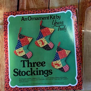 May include: An ornament kit by Yours Truly, featuring three patchwork stocking designs. The kit includes instructions and materials for making three Christmas stockings.