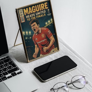May include: A framed comic book cover featuring a football player in a red jersey with the text "MAGUIRE HEADS UNITED TO THE FINALS" and "Snapdragon" on the cover.