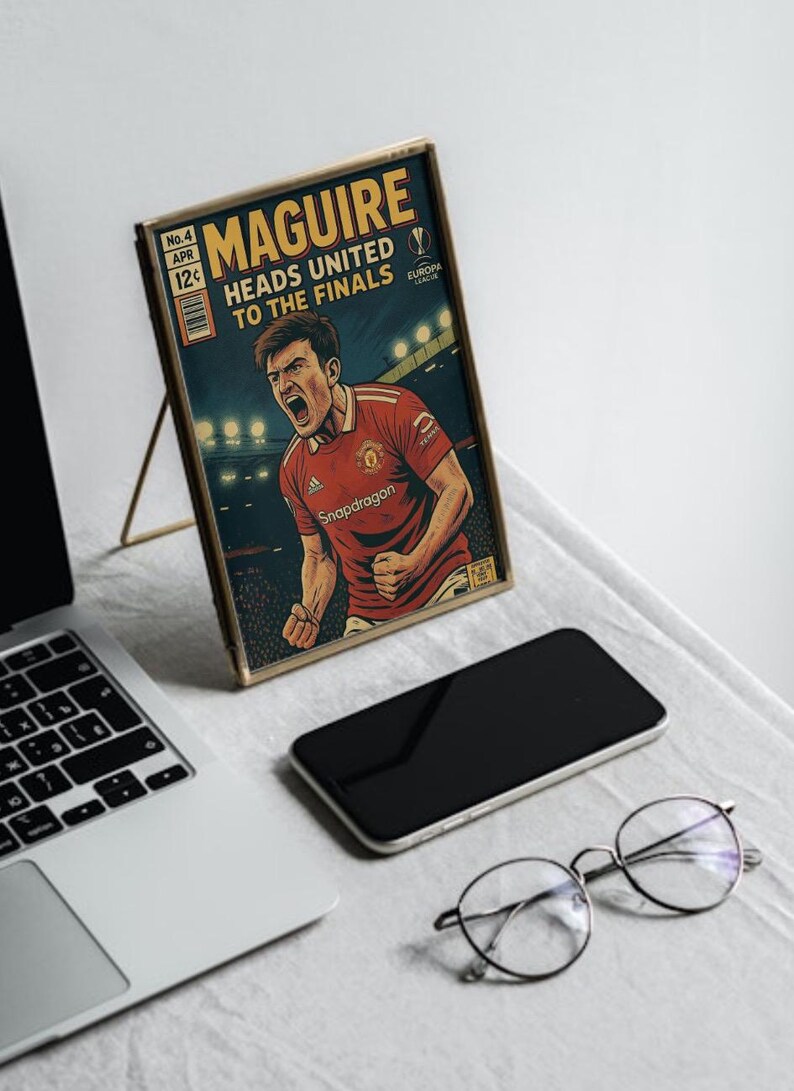 May include: A framed comic book cover featuring a football player in a red jersey with the text "MAGUIRE HEADS UNITED TO THE FINALS" and "Snapdragon" on the cover.