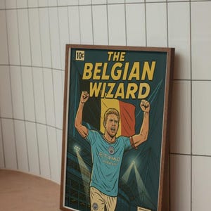 Könnte beinhalten: Gerahmter Druck im Comic-Stil mit dem Titel "The Belgian Wizard". Das Kunstwerk zeigt einen Fußballspieler in einem hellblauen Trikot, der eine belgische Flagge hält. Der Druck hat einen dunklen Holzrahmen und steht vor einer weißen Fliesenwand.