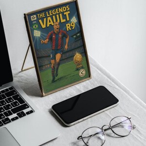 K&ouml;nnte beinhalten: Ein gerahmtes Comic-Cover mit einem Fu&szlig;ballspieler in einem rot-blauen Trikot mit dem Text "The Legends Vault R9" auf dem Cover.