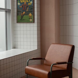 K&ouml;nnte beinhalten: Ein gerahmtes Poster mit einem Vintage-Comic-Design, das einen Fu&szlig;ballspieler in einem rot-wei&szlig;en Trikot zeigt. Das Poster tr&auml;gt den Titel "The Legends Vault R9" und h&auml;ngt an einer wei&szlig;en gekachelten Wand neben einem braunen Ledersessel.