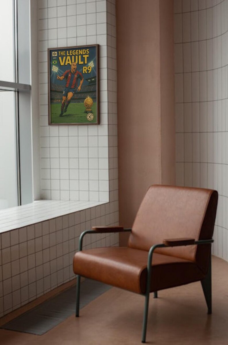 K&ouml;nnte beinhalten: Ein gerahmtes Poster mit einem Vintage-Comic-Design, das einen Fu&szlig;ballspieler in einem rot-wei&szlig;en Trikot zeigt. Das Poster tr&auml;gt den Titel "The Legends Vault R9" und h&auml;ngt an einer wei&szlig;en gekachelten Wand neben einem braunen Ledersessel.