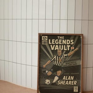 May include: Framed vintage-style print featuring a soccer player in a black and white striped uniform kicking a ball. The print reads "The Legends Vault" and "Alan Shearer" with "Newcastle Saint James Park" text.