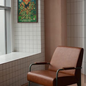 Pu&ograve; includere: Una poltrona in pelle marrone con struttura in metallo e braccioli in legno. La poltrona &egrave; di fronte a una parete piastrellata bianca con un poster incorniciato che recita "Champions Again!"  Celtic Crowned Champions 9th Time in a Row.