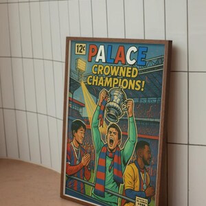 Puede incluir: Una impresión enmarcada al estilo cómic con el texto "PALACE CROWNED CHAMPIONS!". Representa a un equipo de fútbol celebrando una victoria. La obra utiliza colores vibrantes y un estilo retro, con un estadio de fondo.