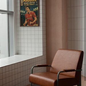 May include: A vintage-style comic book cover featuring a soccer player in a red jersey with the text "MAGUIRE HEADS UNITED TO THE FINALS" printed on the cover. The comic book cover is framed and hanging on a wall.