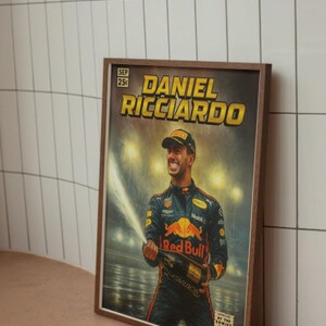 Puede incluir: Impresi&oacute;n enmarcada al estilo c&oacute;mic que presenta a Daniel Ricciardo celebrando con champ&aacute;n. La obra de arte tiene una est&eacute;tica vintage con el texto "DANIEL RICCIARDO" en amarillo. La impresi&oacute;n est&aacute; en un marco de madera marr&oacute;n.