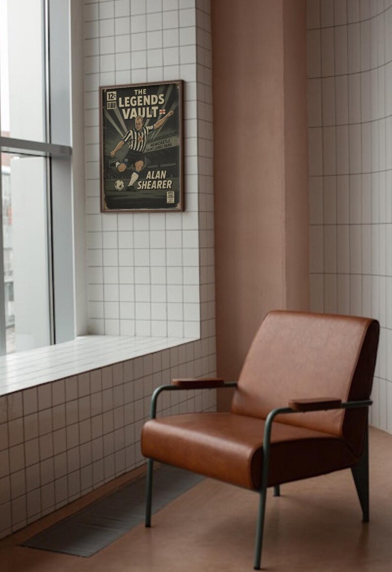 May include: A framed vintage poster titled "The Legends Vault" featuring Alan Shearer in a soccer action pose. A brown leather armchair with metal legs sits in front of a tiled wall and window.