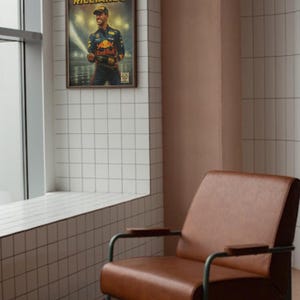 Puede incluir: Un p&oacute;ster enmarcado con Daniel Ricciardo, piloto de F&oacute;rmula 1, sosteniendo una botella de champ&aacute;n. El p&oacute;ster tiene un estilo vintage con un marco marr&oacute;n y est&aacute; colgado en una pared de azulejos blancos. Cerca hay un sill&oacute;n de cuero marr&oacute;n con patas de metal.