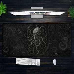 May include: A large black desk mat featuring a detailed illustration of an octopus-like creature with swirling tentacles and a starry background. A white keyboard and mouse are visible below the mat. A computer monitor and plants are above.