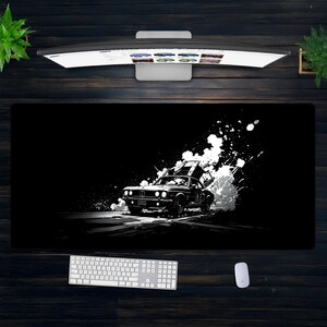 Puede incluir: Alfombrilla de escritorio en blanco y negro con un coche clásico en movimiento, con efectos de salpicaduras de pintura blanca. El coche es el punto focal, sobre un fondo oscuro. Un teclado y un ratón son visibles en la parte inferior.