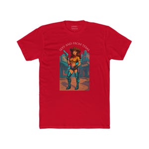May include: Red t-shirt featuring a graphic of a cowgirl holding a gun, with the text "Sexy and From Texas." The cowgirl is wearing a brown hat, yellow top, and blue shorts. The shirt has the text "JAMES SMITH" at the top.