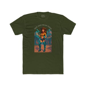 May include: Olive green t-shirt featuring a graphic of a woman in a cowboy outfit holding a gun, with the text "Sexy and From Texas". The illustration is set against a saloon backdrop.