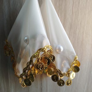 May include: Two white sheer fabric cones suspended by a gold chain. The bottom edges are trimmed with a decorative gold scalloped border featuring dangling gold-toned coin charms and a single white pearl accent on each piece of fabric.
