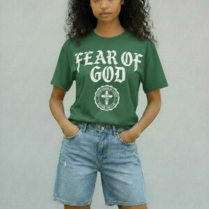May include: A green t-shirt with the text "FEAR OF GOD" in white, along with a circular emblem. The model is wearing light blue denim shorts. The overall style is casual and modern.