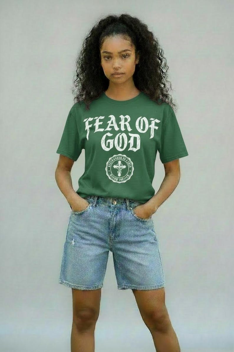 May include: A green t-shirt with the text "FEAR OF GOD" in white, along with a circular emblem. The model is wearing light blue denim shorts. The overall style is casual and modern.